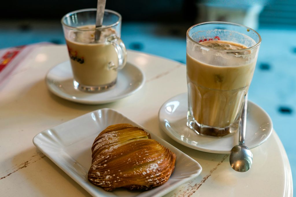 Sfogliatella dessert pastry on a white plate, with two iced coffees next to it. 