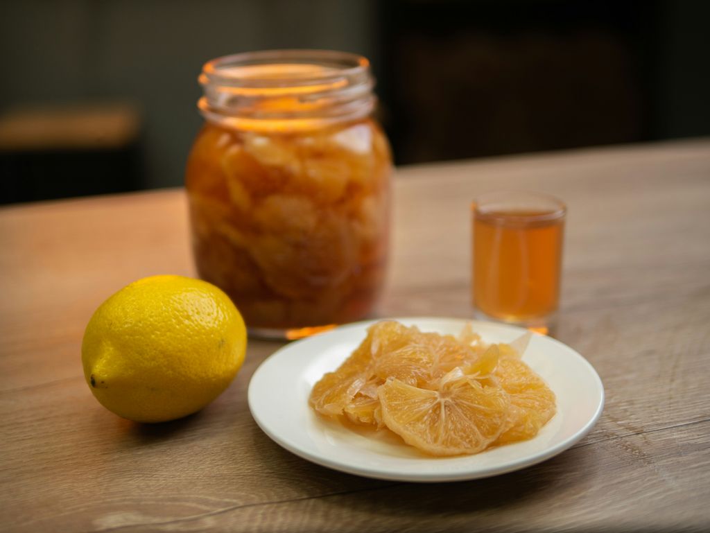 a jar of limoncello with a yellow lemon next to it, and a small cup of limoncello