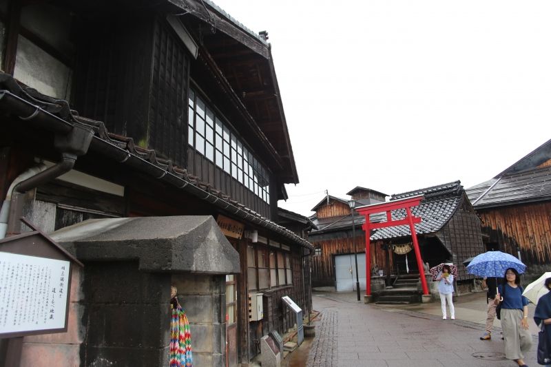 Niigata Private Tour - Koshino Murasaki soy sauce brewery wooden building on the left side is on ancient Mikuni Highway protected by local Inari Shrine with vermillion-colored torii gate on the right side.