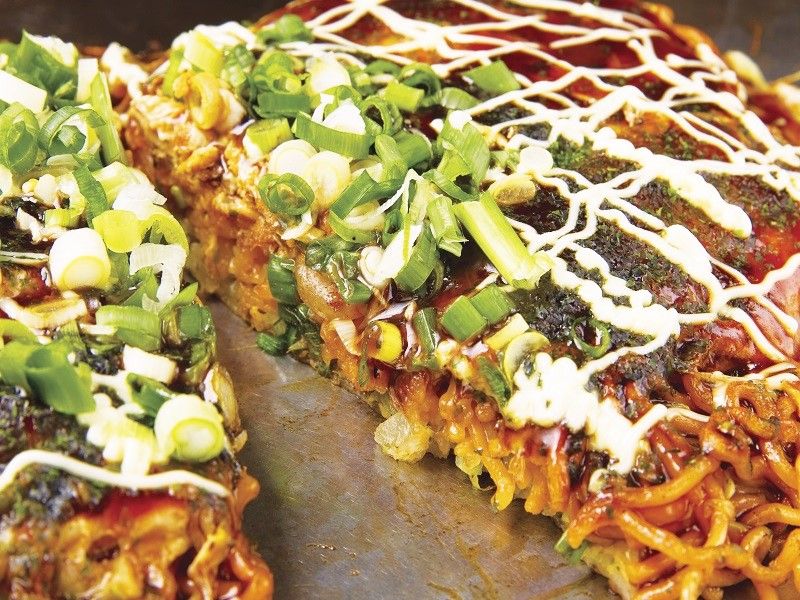 Plenty of sauce goes onto the piping-hot okonomiyaki which has noodles pressed inside!
