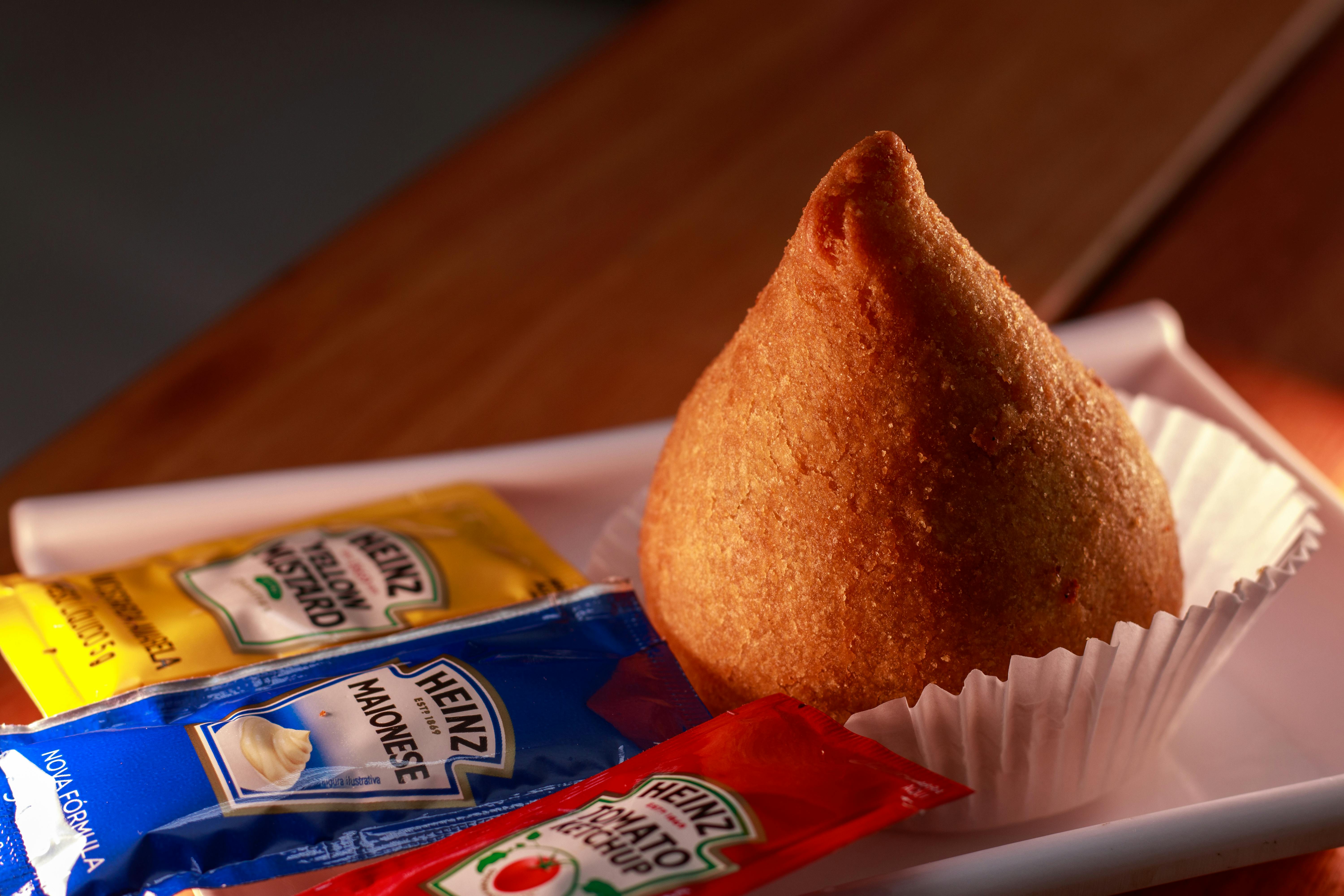 one Coxinha potato roll with a ketchup, mayonnaise and mustard packet next to it. 